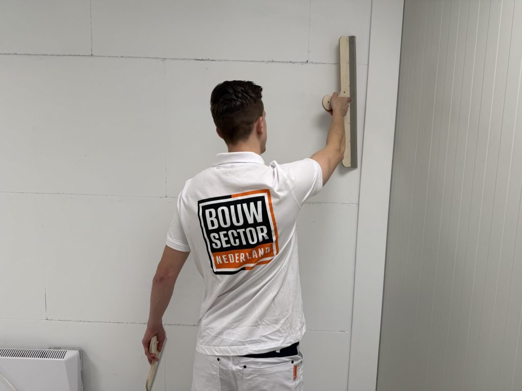 Stukadoor van dichtbij gezien terwijl hij een lange spaan tegen de bovenkant van een wand houdt