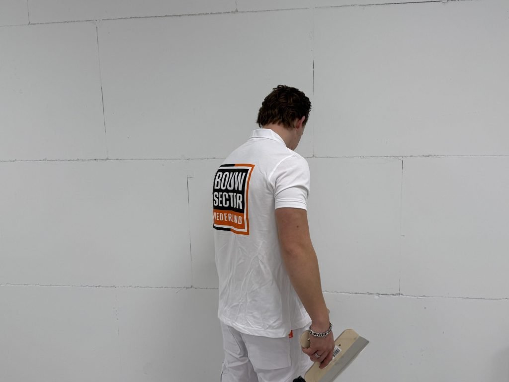 Stukadoor van Bouwsector Nederland bekijkt een kale wand met plaatnaden, met een plakspaan in zijn hand