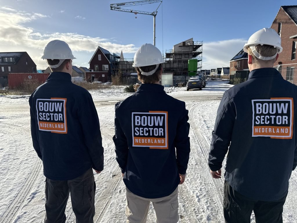 Drie vakmensen van Bouwsector Nederland met witte helm op een besneeuwd nieuwbouwterrein met een bouwkraan